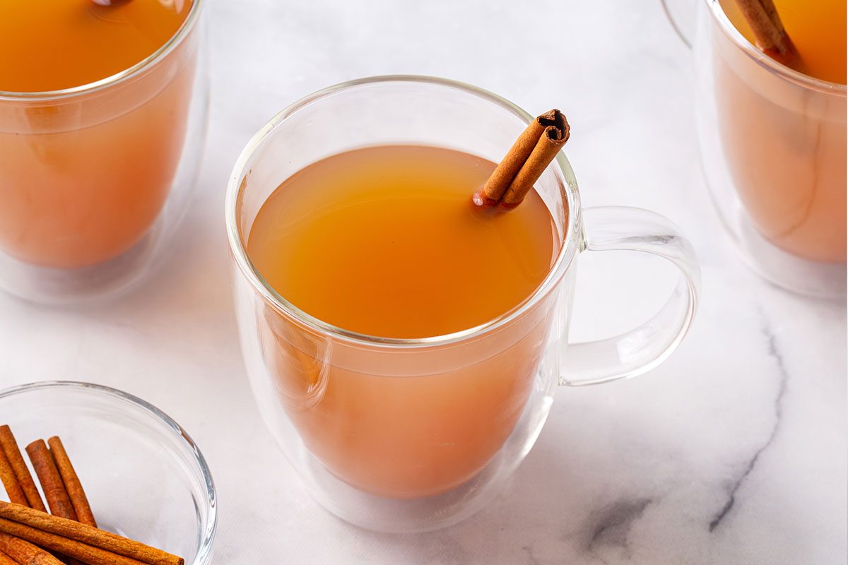 Hot Apple Cider in clear mug glasses with a cinnamon stick for Taste of Home