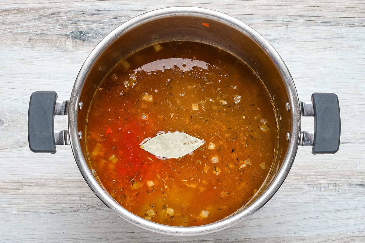 The lentils, broth, crushed tomatoes., seasonings and bay leaf are added to the Instant Pot in preparation for pressure cooking.