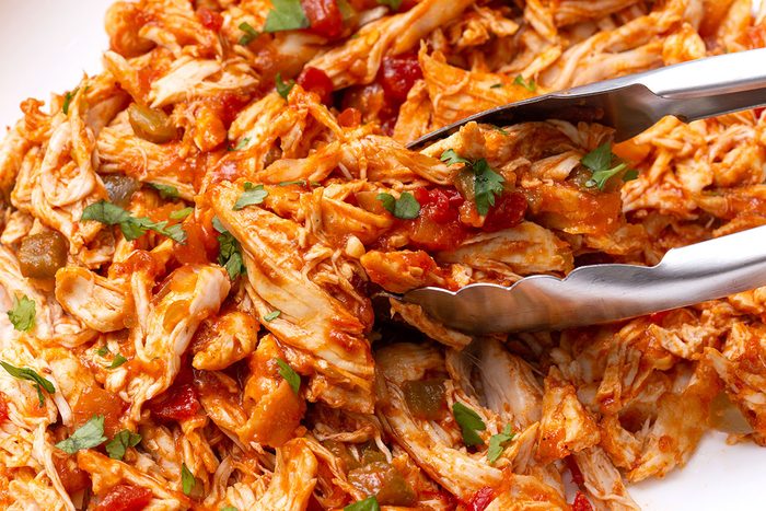 A portion of Instant Pot Salsa Chicken being scooped up with tongs on a serving plate for Taste of Home