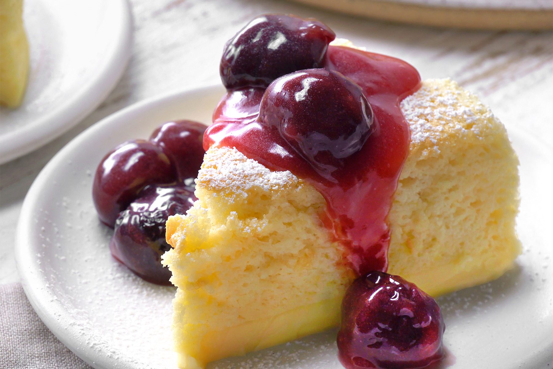 close shot of a slice of Japanese Cheesecake is presented on a white plate, topped with a generous dollop of cherry compote, The cherry compote adds a vibrant burst of color and a sweet, tangy flavor;