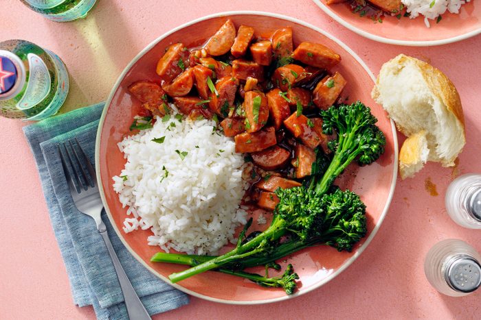 A dish containing Keilbasa and rice served on a plate with fresh green leafy vegetable