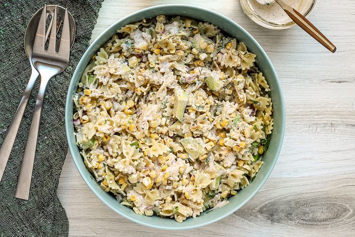 A large bowl of Mexican street corn pasta salad with avocado, charred corn kernels, cilantro, jalapeno pepper, and Cotija cheese.