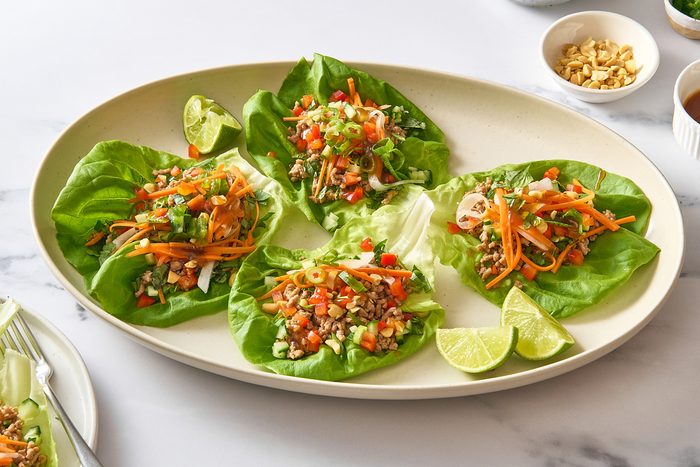 Angled shot of some pork lettuce wraps on a platter, topped with several of the optional garnishes