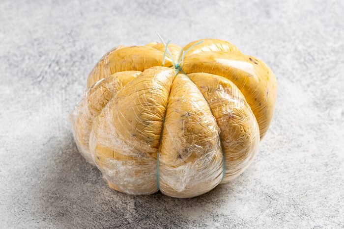 Taste of Home Pumpkin Cheese Ball photo of the cheese ball wrapped in four pieces of string (or four rubber bands), creating indentions to resemble a pumpkin