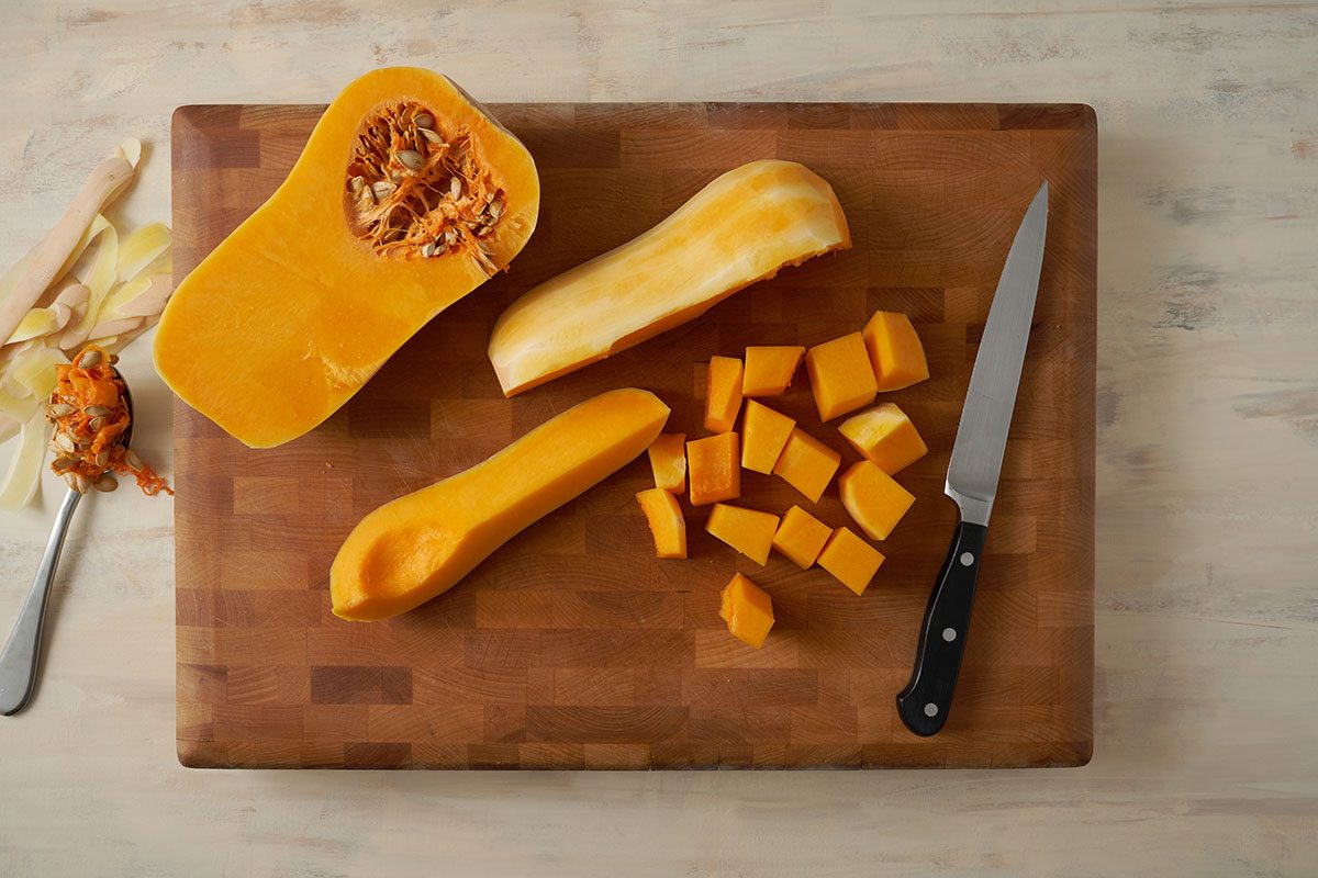Overhead view of butternut squash being peeled and cut into cubes and halves for the Taste of Home Roasted Vegetables with Walnuts recipe.