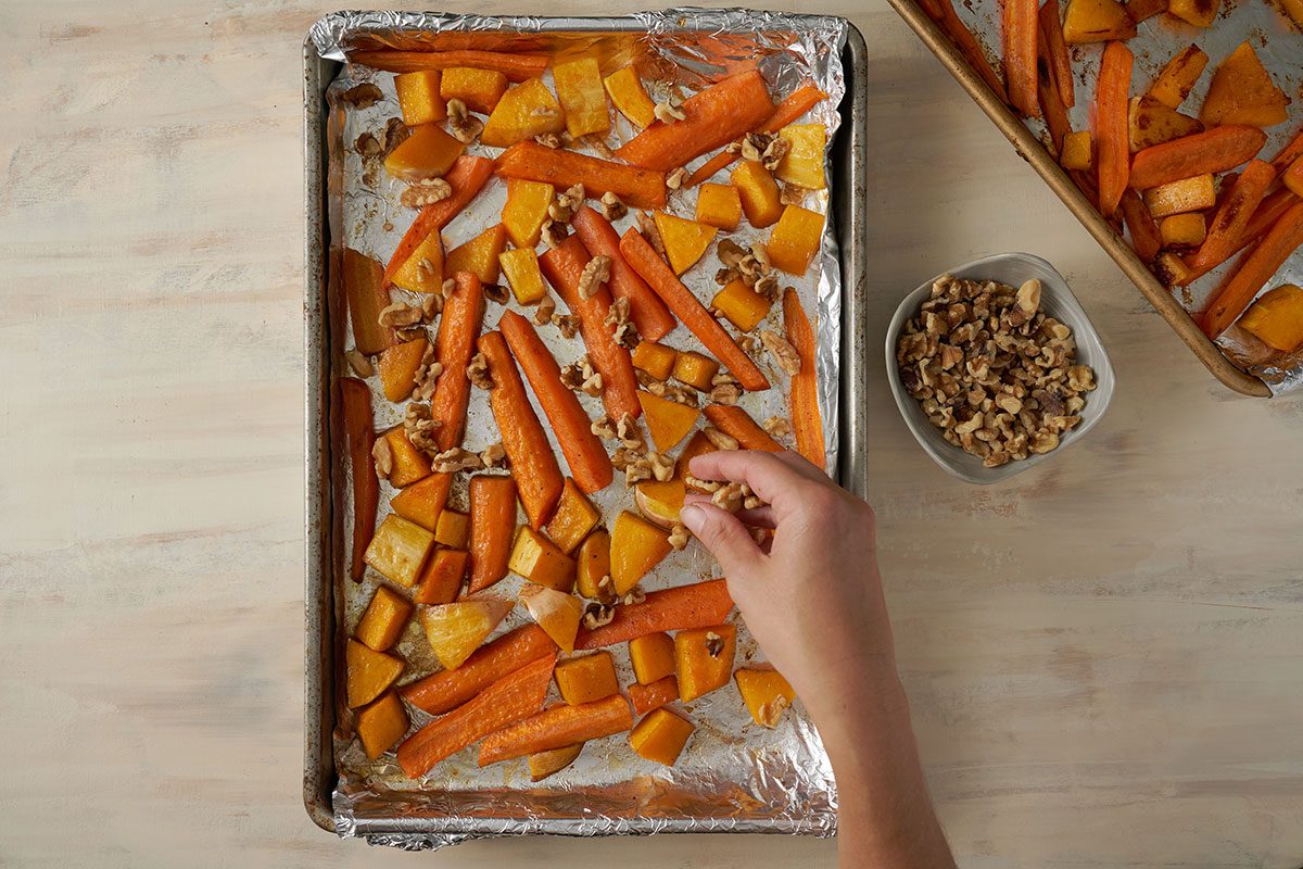 Overhead view of chopped walnuts being sprinkled over the roasted butternut squash and carrots, finishing the dish in the oven for the Taste of Home Roasted Vegetables with Walnuts recipe.