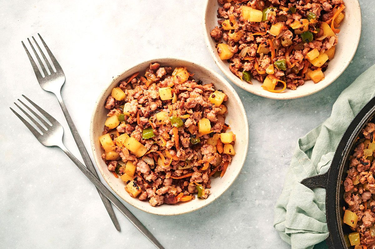 Sausage Hash in two bowls on a marble table next to a cast iron skillet, recipe by Taste of Home