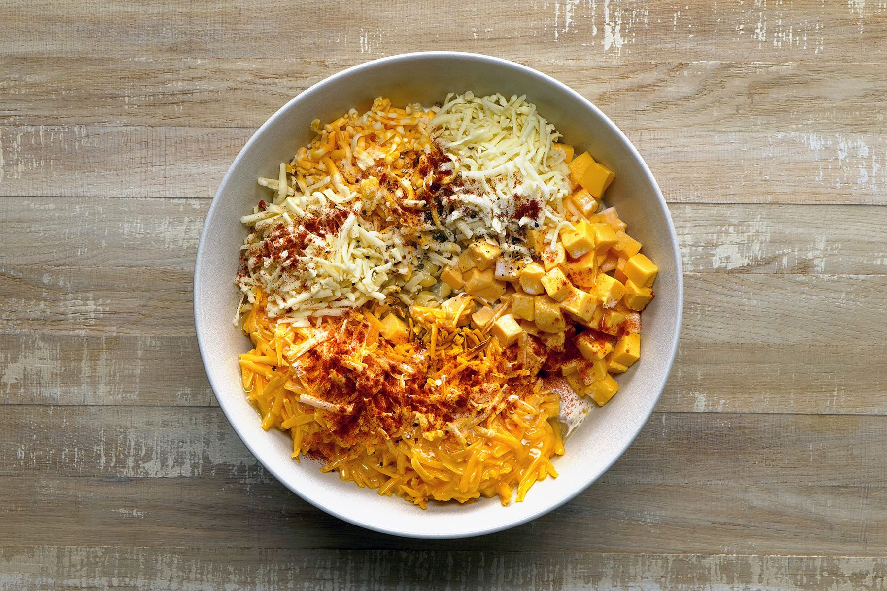 Velveeta, smoked cheddar, cheddar cheese, milk, eggs, heavy cream, half-and-half, provolone, Colby-Monterey Jack, pepper jack, salt, pepper, paprika added to pasta in a bowl.