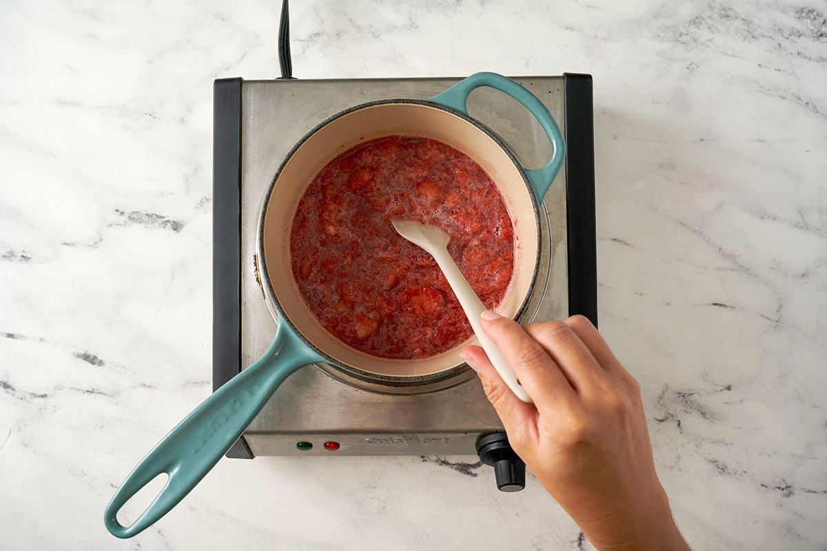 Gradually adding mashed unsweetened strawberries to the syrup base, simmering until the strawberries break down and the syrup thickens, for the Strawberry Syrup recipe, by Taste of Home.