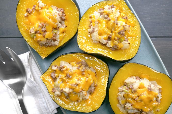 overhead shot of Four acorn squash halves are filled with a mixture of ground meat, rice, and cheese, The meat mixture is a golden brown color and is topped with melted cheese, The acorn squash shells are a vibrant orange color and are still attached to the stems, The squash halves are arranged on a blue platter, and two forks are placed next to the platter;