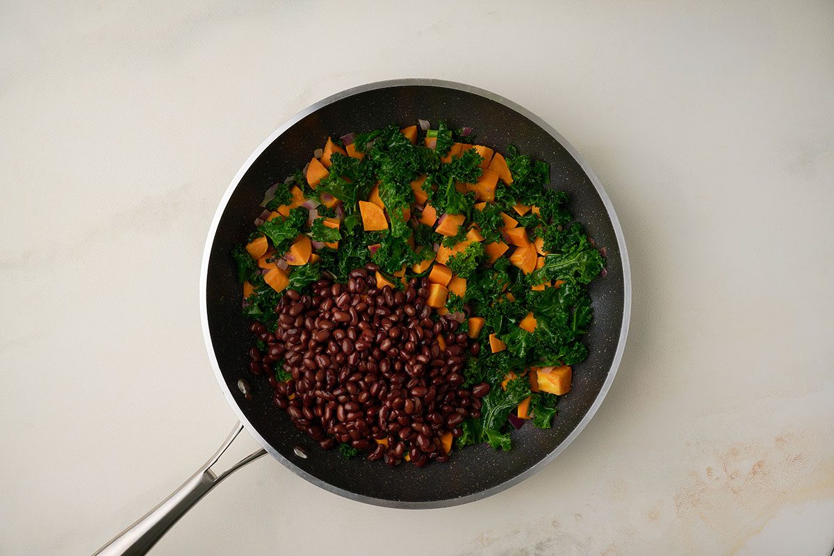 Overhead shot of Kale and Black Beans added to skillet for Sweet Potato Bowl