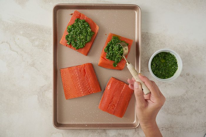 Overhead view of salmon fillets in a greased baking dish, being topped with homemade pesto, ready to bake for the Taste of Home Basil Salmon recipe.