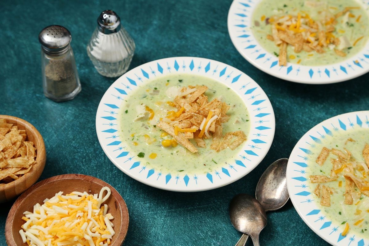 Close up of Taste of Home's Poblano Soup served in blue and white bowls on a teal surface.