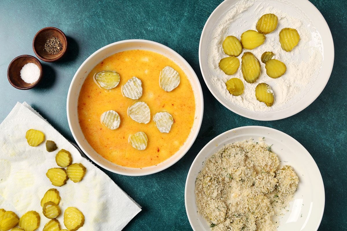 Process of making Taste of Home's Oven Fried Pickles on a wire rack and baking sheet on a teal surface.