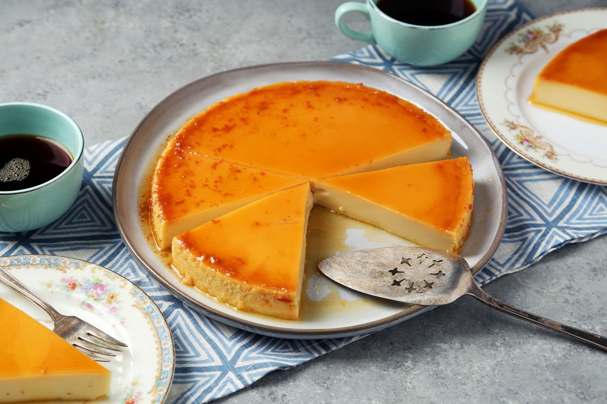 Close up of Taste of Home's Flan de Queso cut and served on plates on a grey surface.
