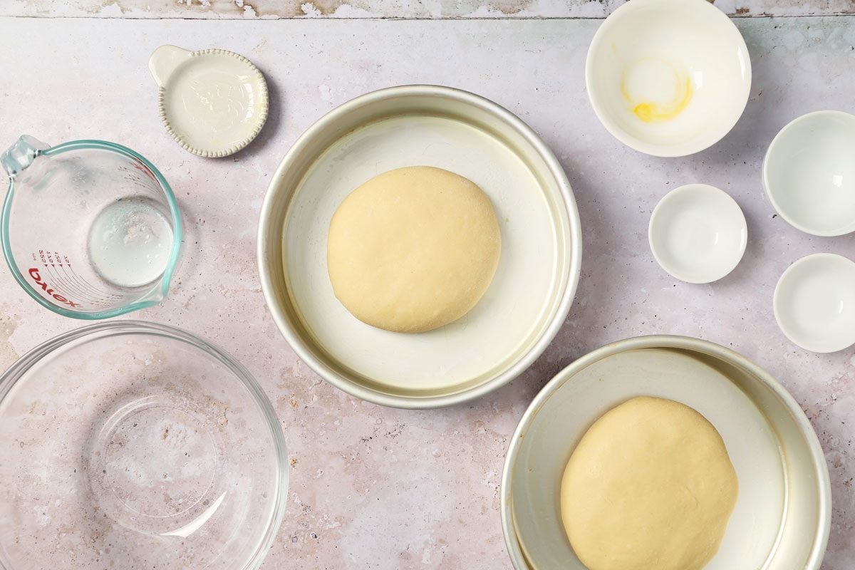 Process of making Taste of Home's Italian Sweet Bread loaves rising in round cake pans on a grey and beige surface.