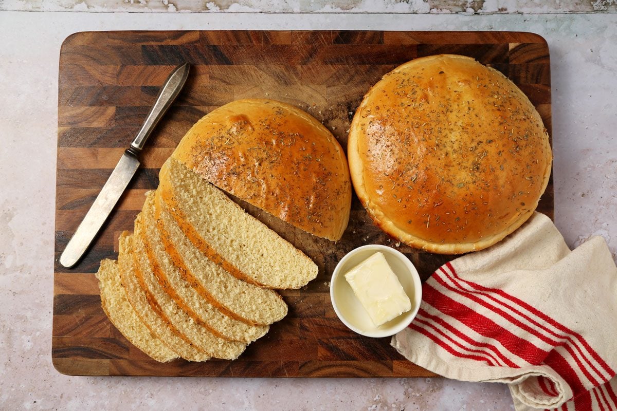 Close up of Taste of Home's Italian Sweet Bread sliced on a wooden cutting board with butter on a grey and beige surface.