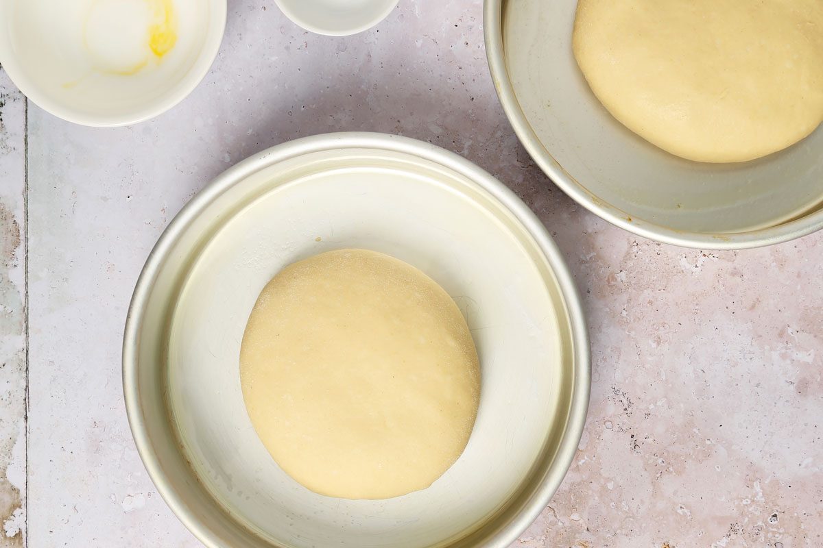 Process of making Taste of Home's Italian Sweet Bread loaves rising in round cake pans on a grey and beige surface.