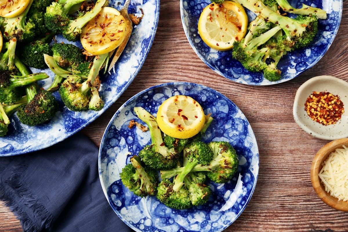 Close up of Taste of Home's Grilled Broccoli served on blue plates and a platter on a brown wooden surface.