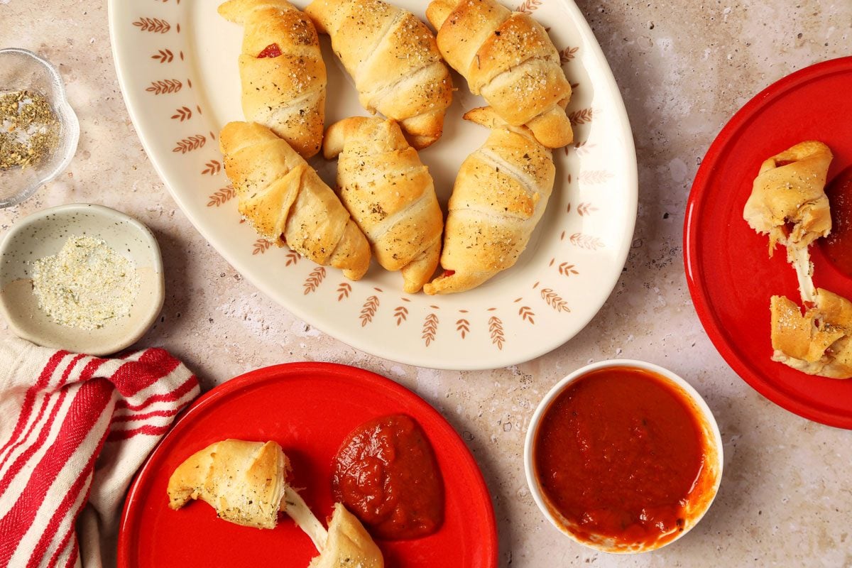 Close up of Taste of Home's Pepperoni Rolls served on a platter and red plates on a brown and beige marble surface.