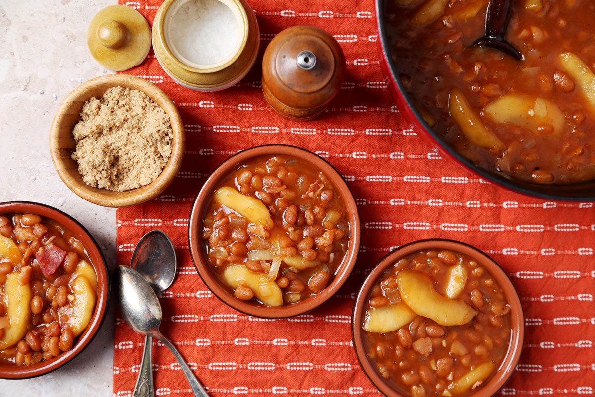 Close up of Taste of Home's Apple Pie Baked Beans served in small brown dishes on an orange towel on a brown marble surface.