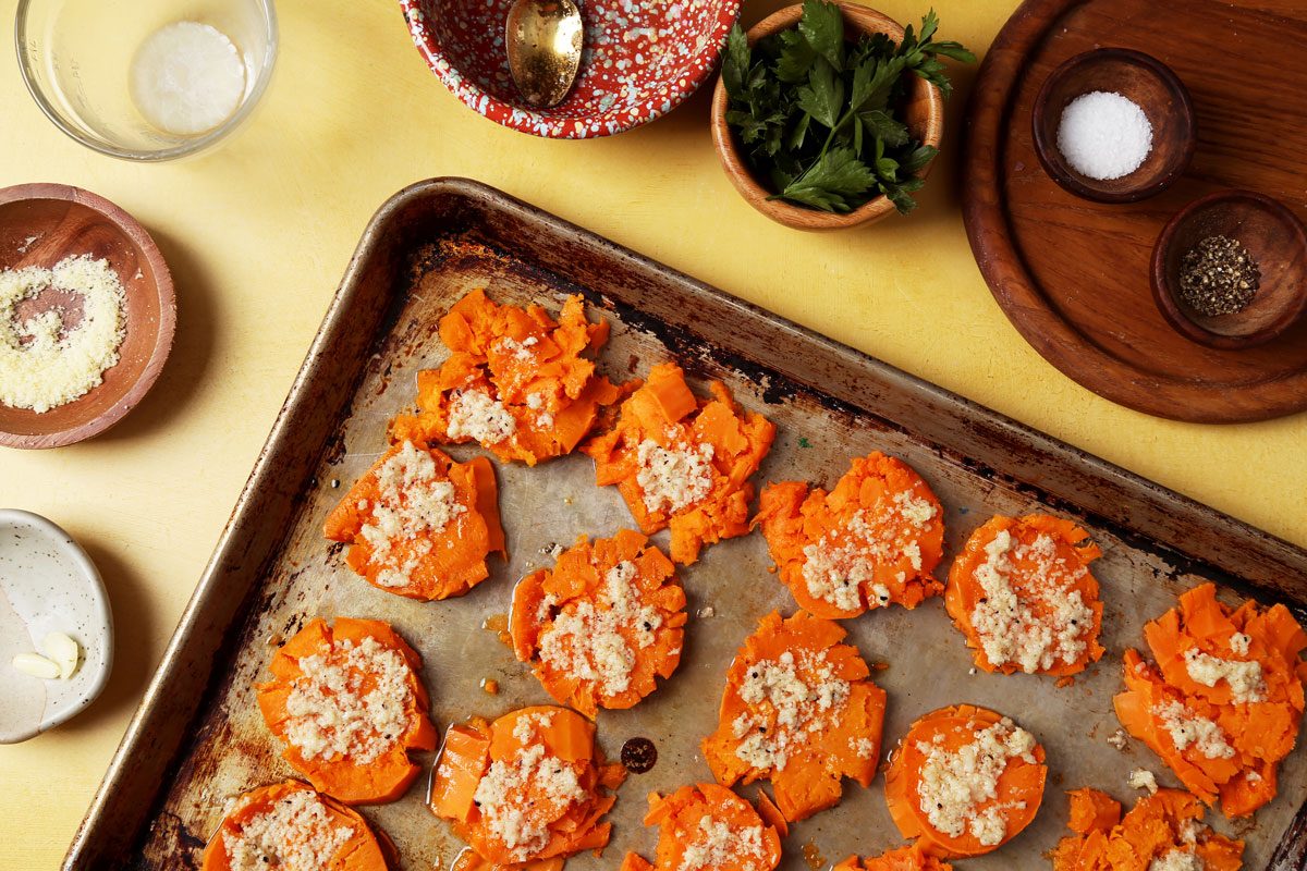Process of making Taste of Home's Smashed Sweet Potatoes on a large baking sheet on a yellow surface.