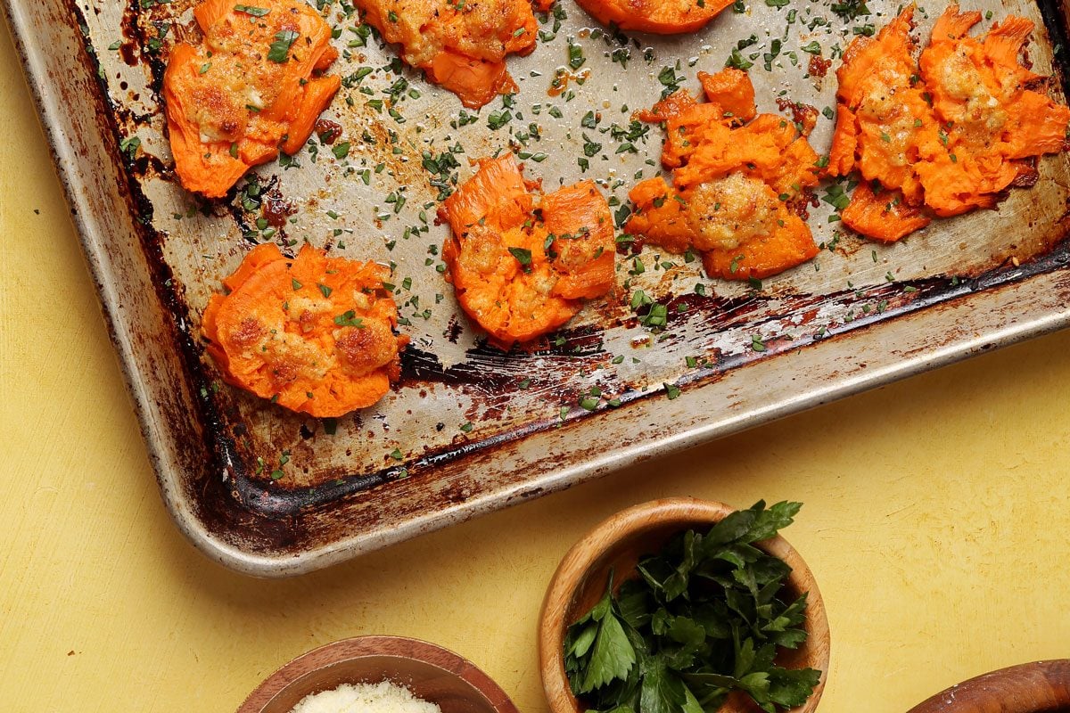 Close up of Taste of Home's Smashed Sweet Potatoes on a large baking sheet on a yellow surface.