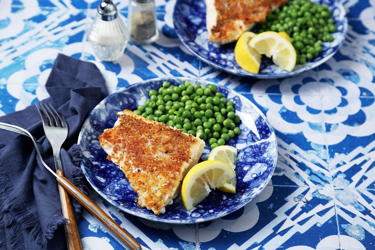 Close up of Taste of Home's Pan-Seared Red Snapper on a blue plate with peas and lemon slices on a blue and white tiled background.