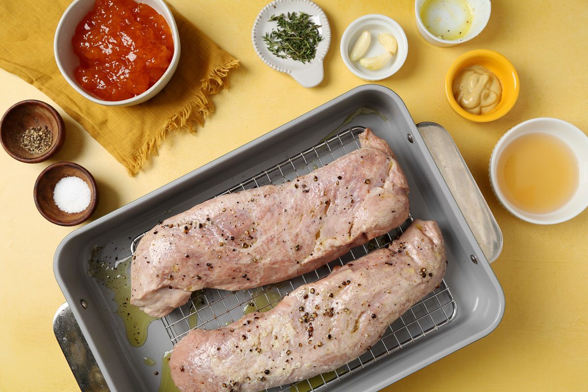 Process of making Taste of Home's apricot glazed pork tenderloin roasting on a roasting rack on a yellow surface.