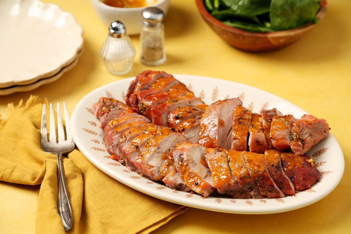 Close up of Taste of Home's apricot glazed pork tenderloin sliced and served on a large plate on a yellow surface.