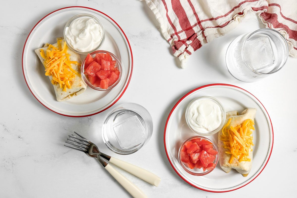 Taste of Home Taco Burrito on enamel plates with bowls of sour cream and tomatoes