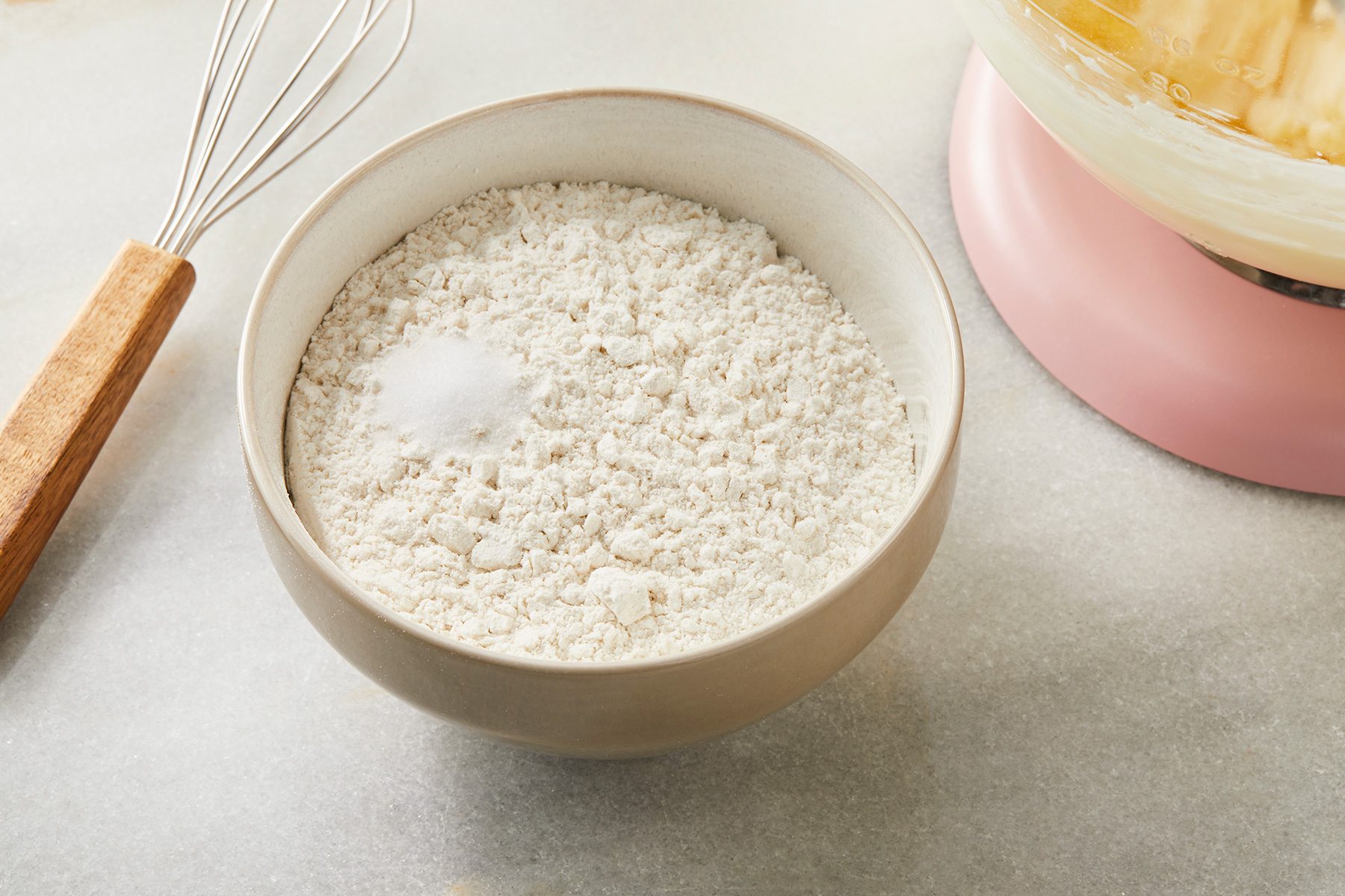 3/4th shot of a small bowl placed over white background; whisking together flour and salt;