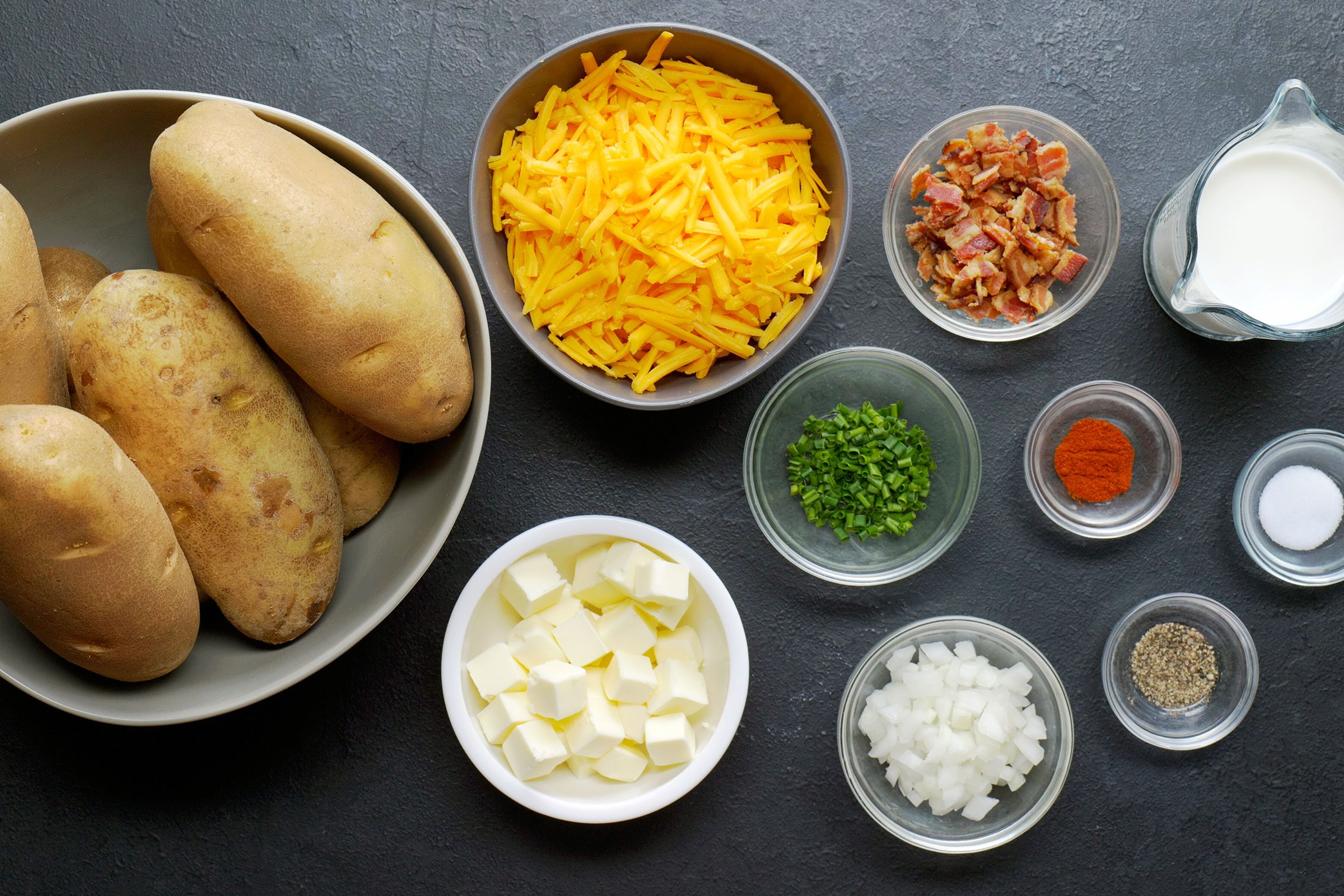 Potatoes, butter and milk, onion and chives, cheddar cheese, paprika, bacon in bowls