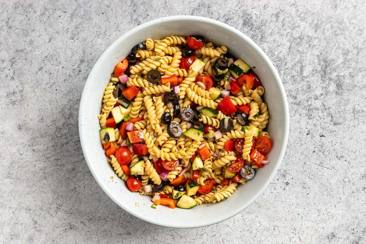 Taste of Home Vegan Pasta Salad photo of all the veggies and pasta in a mixing tossed with the dressing.