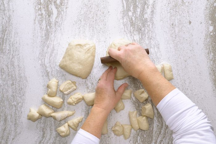 Hands are cutting and portioning dough into small pieces on a floured marble surface.