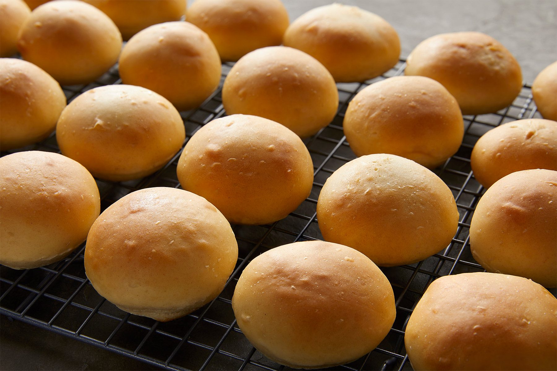 Rows of freshly baked golden brown rolls cooling on a wire rack.