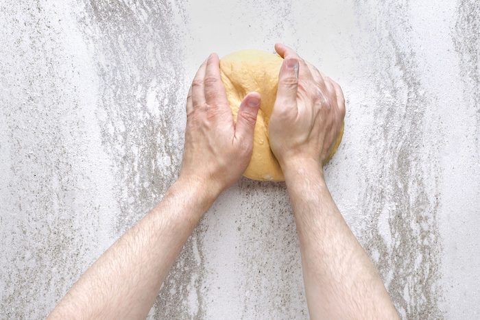 Hands kneading dough on a lightly floured surface.