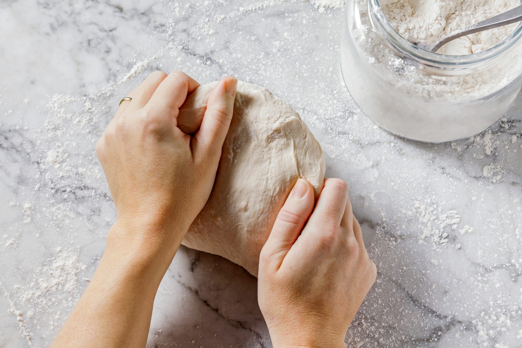 Overhead shot of turning dough onto a floured marble surface; kneading for 6-8 minutes until smooth and elastic.
