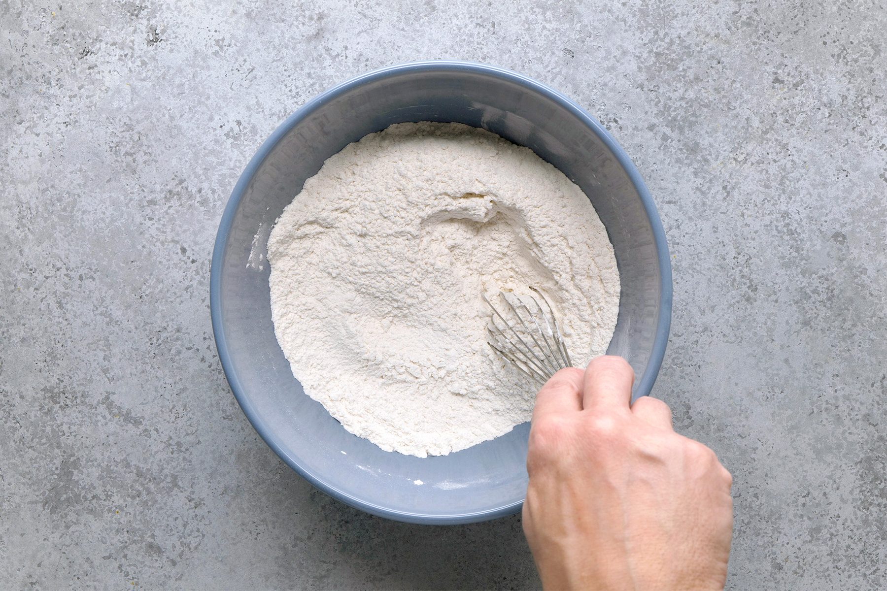 Overhead shot of a large bowl; whisk flour; baking powder; sugar and salt; grey surface;