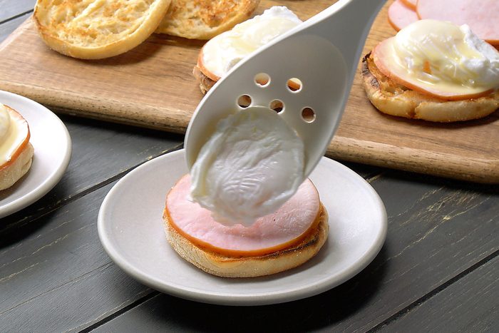 Assembling egg benedict recipe with bacon, hollandaise sauce and poached eggs