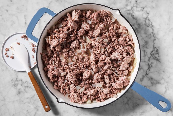 A pan with browned ground beef on a marble countertop. A white spatula with a wooden handle rests nearby.