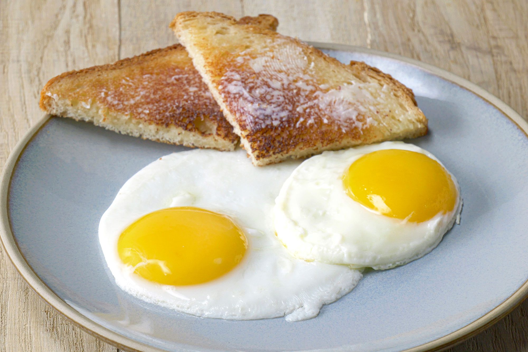 Close shot of Fried Eggs; serve on plate with bread toasts; wooden surface;