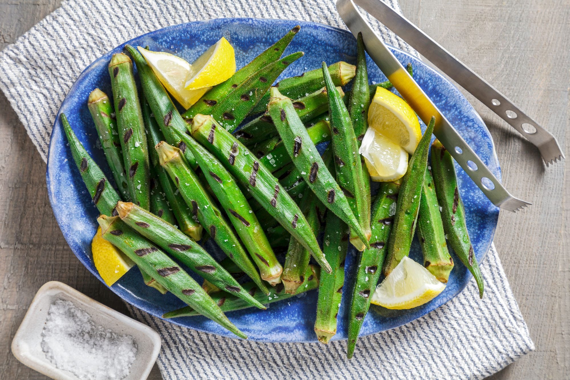 Overhead shot; remove grilled okra from skewers and place on a platter; garnish with lemon juice and salt; serve hot; napkin; wooden surface;