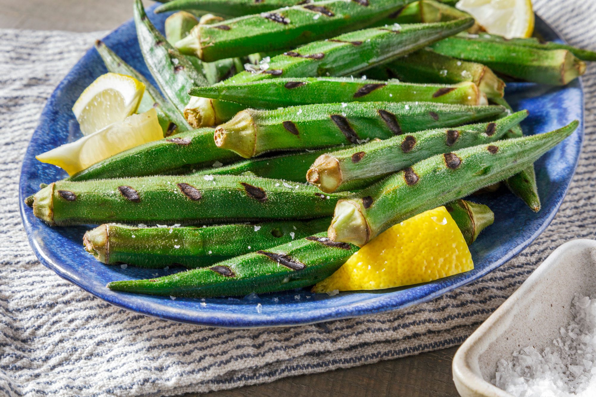 Close shot of Grilled Okra; serve hot on plate; garnish with lemon juice and salt; napkin; wooden surface;