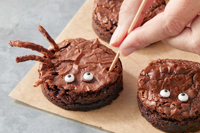 Poking holes in round brownie and adding chocolate coated noodle legs