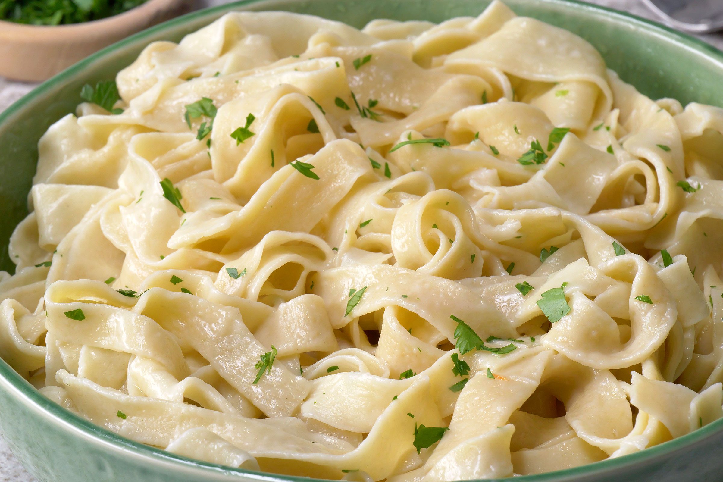 Egg noodles sprinkled with parsley served in a green bowl