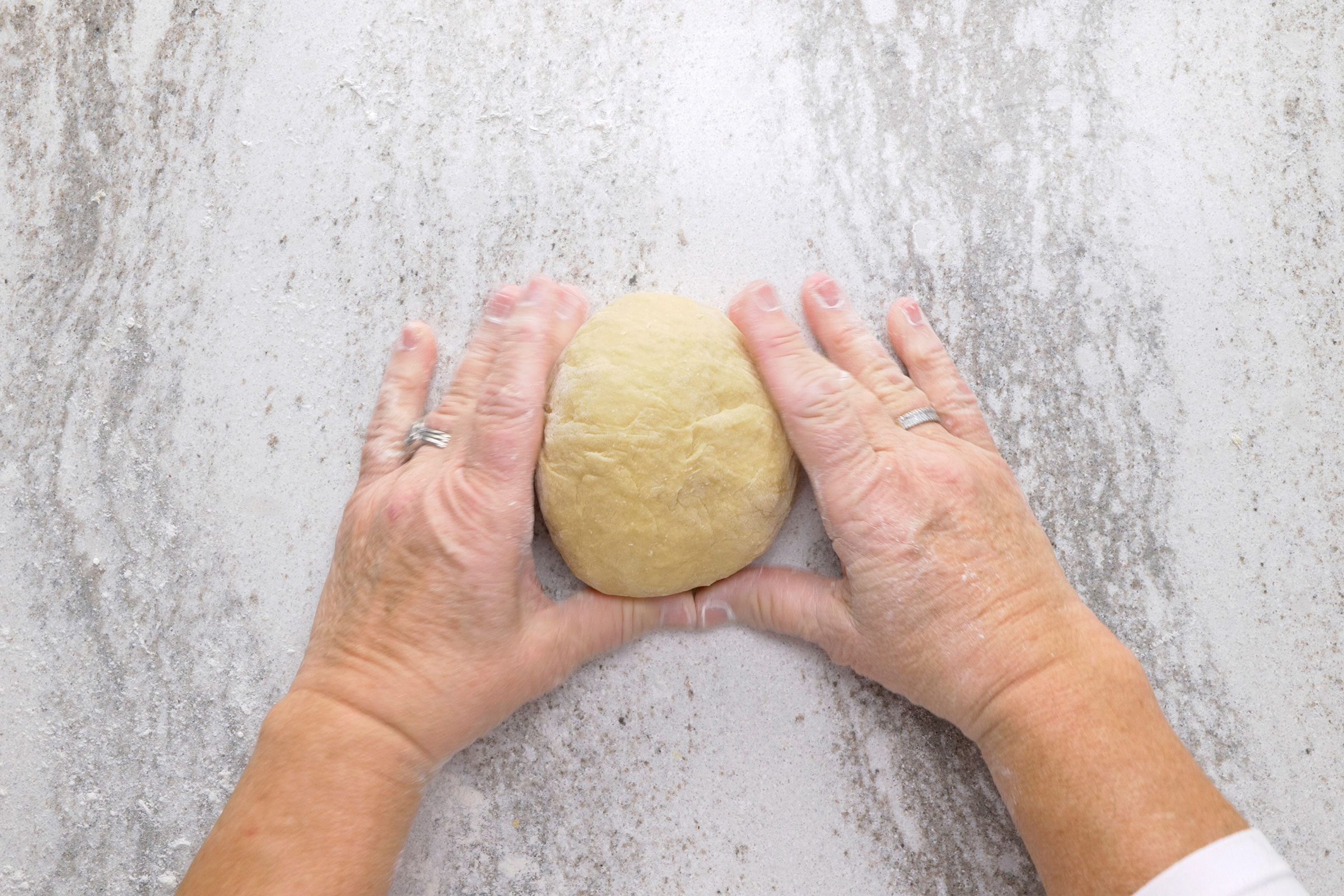 Both hands holding gathered dough shaped into a ball