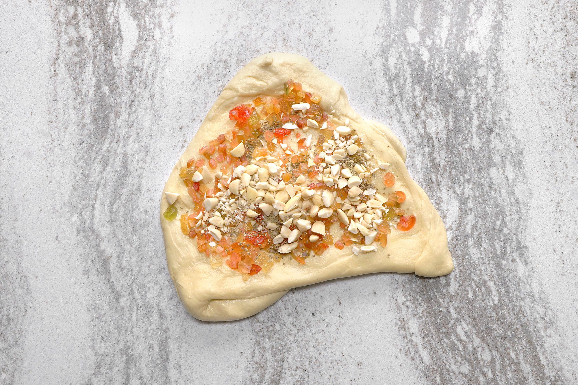 overhead shot of a triangle shaped piece of dough on a white surface; the dough is covered with almonds and candied fruit