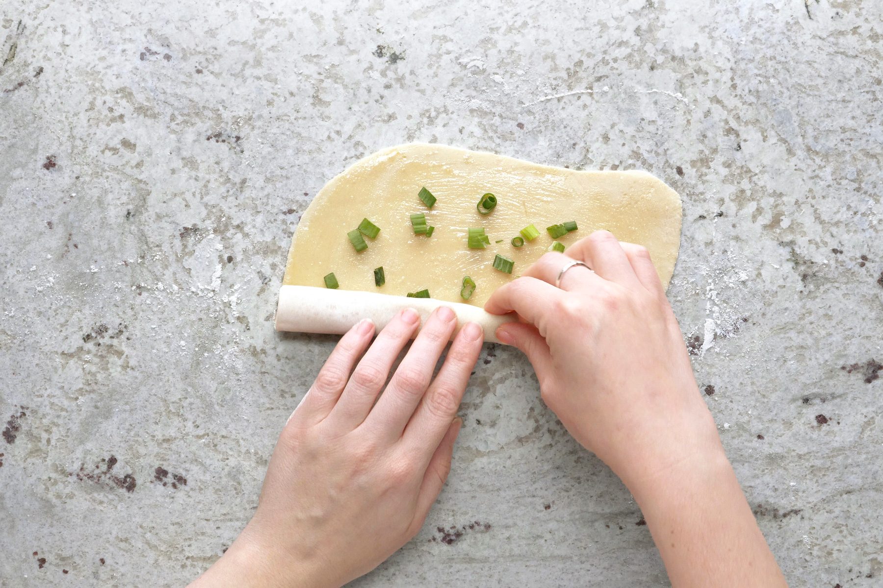 Rolling up the dough after adding salt and chopped green onions.