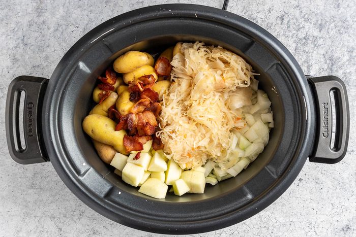 Taste of Home Slow Cooker Pork and Sauerkraut photo of the sauerkraut, potatoes, onion, apple and bacon in the slow cooker.